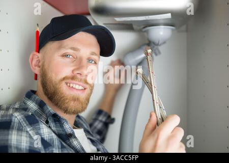 positive plumber fixing under the sink in the kitchen Stock Photo