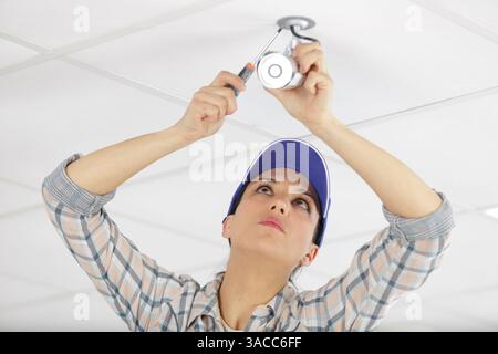 female worker changing spotlight on the ceiling Stock Photo