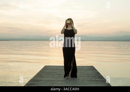 woman with black dress and screen on her face in front of a surreal sunset Stock Photo