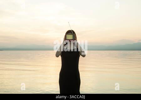 woman with black dress and screen on her face in front of a surreal sunset Stock Photo