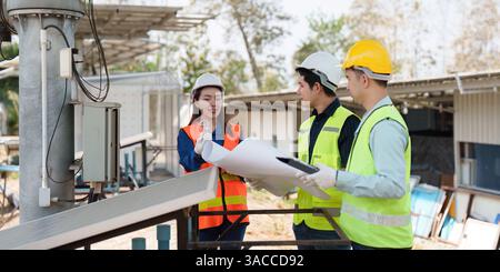 Sustainable Infrastructure and Teamwork. Engineers reviewing plans and discussing the installation of solar panels in an eco-friendly setting. Stock Photo