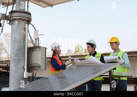 Renewable Energy and Collaboration. Professionals discussing solar panel installation while reviewing detailed plans on-site. Stock Photo