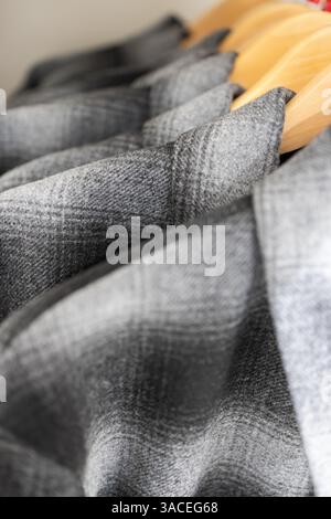 Close-up of gray plaid men’s shirts on wooden hangers with a focus on the checkered fabric pattern texture and neatly arranged collars Stock Photo