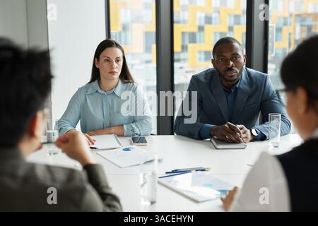 Diverse business team discussing project at meeting table in modern office with focus on female manager listening to colleagues Stock Photo