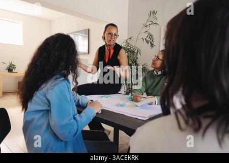 A confident businesswoman engages her team in a meeting focused on discussing project scope. Collaboration and teamwork are emphasized as they work. Stock Photo
