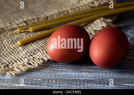 Traditional easter red dyed eggs with beeswax candles on rustic wooden and burlap background Stock Photo