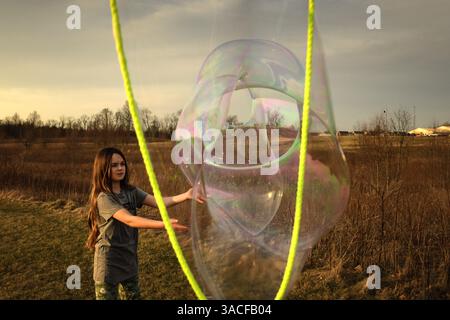 Tween girl popping giant bubble in sunny field Stock Photo