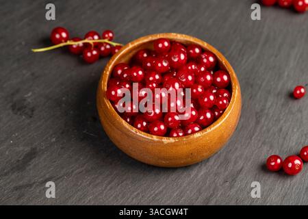 ripe red currant berries poured in a wooden bowl, harvest small red currant berries on the kitchen table in a bowl, closeup Stock Photo