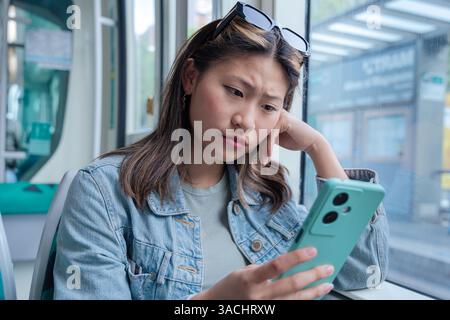 Young Chinese woman looking concerned while reading phone on public transport Stock Photo