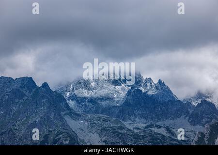 Beautiful view of mountains covered by clouds. Dramatic sky clouds, snowy peaks with overcast view. Artistic hiking landscape, abstract background Stock Photo