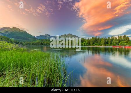 Awesome nature landscape. Beautiful scene with high Tatra mountain peaks, rocks in mountain lake, calm lake water, reflection, colorful sunset sky Stock Photo