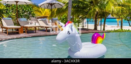 Inflatable pool toys at tropical resort pool, relaxing in infinity pool with ocean view under palm trees. Poolside chairs umbrellas and relaxation Stock Photo