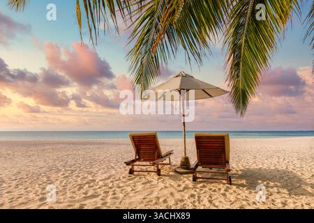 Sunset views tropical beach chairs umbrella on golden sand, serene turquoise sea, palm trees under vibrant colorful sky. Romantic honeymoon landscape Stock Photo