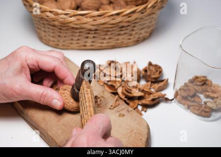 Hands cracking a walnut with a small hammer on a wooden board. Stock Photo