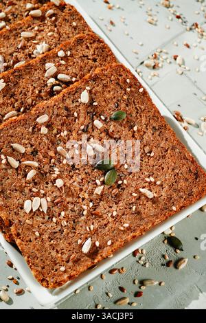 high angle view of some rectangular slices of rye bread with flax seeds, on a a white rectangular ceramic plate, placed on a gray textured surface Stock Photo