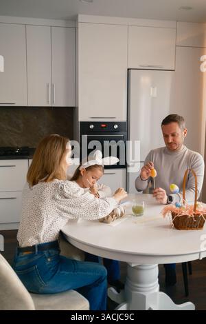 Family decorating Easter eggs together in a modern kitchen setting Stock Photo