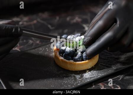Confectioner decorating tasty tart with mint at dark table, closeup Stock Photo