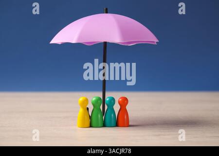 Human figures under umbrella on light wooden table against blue background. Insurance concept Stock Photo