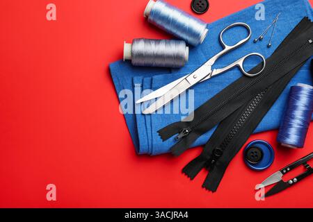 Different sewing supplies on red background, flat lay. Space for text Stock Photo