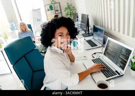 Confident businesswoman working in an office with team, surrounded by computers and code development Stock Photo