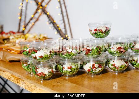 Clear plastic containers filled with arugula, feta cheese, sun-dried tomatoes, and meat, neatly arranged for catering or takeaway. Stock Photo