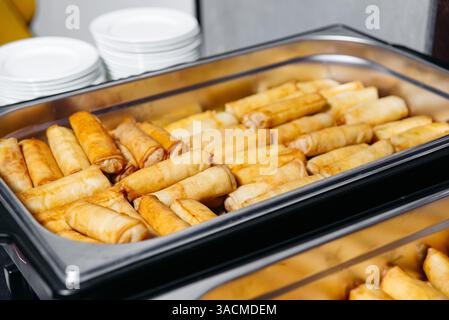 A large serving tray filled with neatly arranged golden brown spring rolls, prepared for a buffet or catering event. Stock Photo