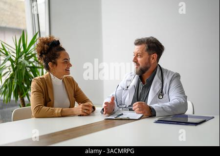 Smiling male doctor holding eyeglasses and discussing medical test results with female patient in clinic Stock Photo