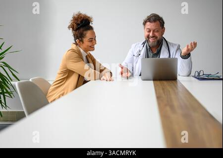 Smiling male healthcare worker explaining medical record to female patient over laptop at desk in office Stock Photo