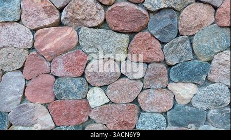 Wall made of irregular round granite stones Stock Photo
