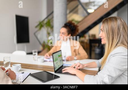 Businesswoman analyzing financial data and performance over laptop while working together in board room Stock Photo