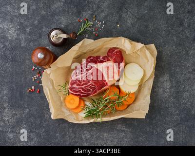 Raw osso buco. Fresh veal cut meat on parchment paper with vegetables and spices on an old concrete table background. Italian cuisine background with Stock Photo