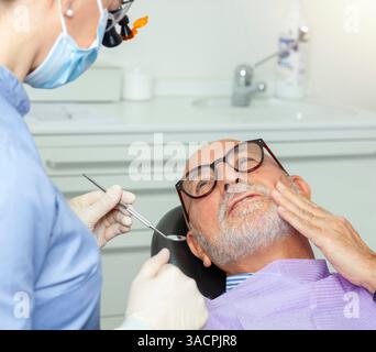 Senior man experiencing toothache during a dental checkup, showing signs of worry while undergoing examination in a clinic Stock Photo
