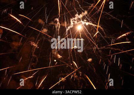 Bright orange and white fireworks exploding in the night sky, creating a spectacular display of light and color Stock Photo