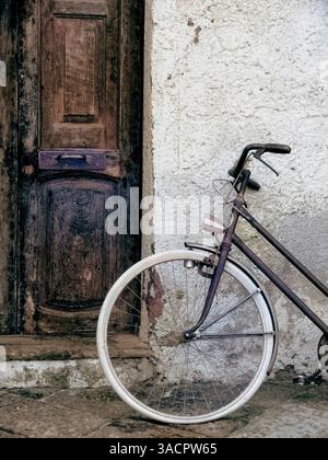 Old bicycle parked against a white wall next to a dark wooden door in a vintage, rustic setting Stock Photo
