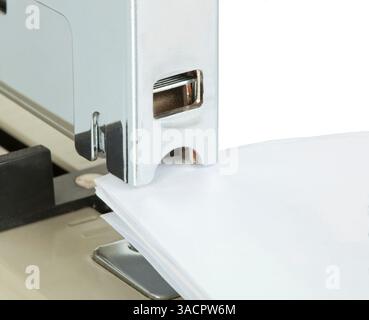 Metallic stapler binding sheets of white paper on white background, close up on the stapler Stock Photo