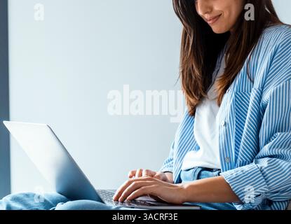 Concentrated young Caucasian freelance businesswoman using laptop at home, sitting on sofa, looking at display, thinking, working, watching, reading content Stock Photo