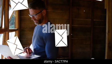 Man using laptop in rustic cabin, managing emails efficiently and focused Stock Photo