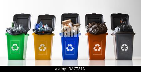 Row of open multi-colored plastic recycling bins filled and overflowing with waste with recycling symbol on a reflective white base and white isolated Stock Photo