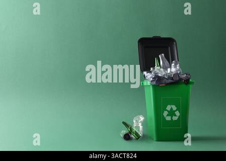 Green trash container with recycling symbol filled with glass objects and containers waste and other glass waste next to it on the ground isolated wit Stock Photo
