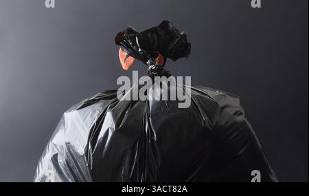 Detail of a full black plastic garbage bag closed with a knot and a dark isolated background. Front view. Stock Photo