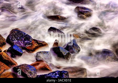 Lava beach rocks worn by centuries of sea water cover the black sand ...