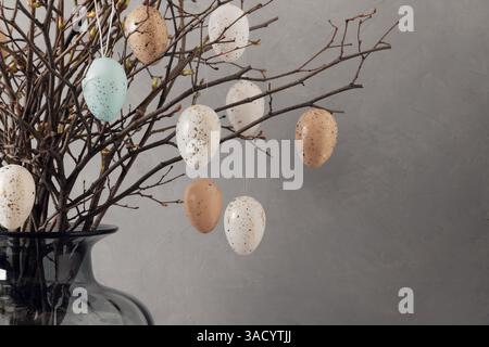 Easter tree decorated colorful pastel white and beige eggs. Birch branches with hang eggs in dark vase on gray background. Vertical format. Happy East Stock Photo