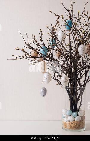 Easter tree decorated white and beige eggs in glass vase on white table. Vertical format. Happy Easter greeting card. Stock Photo