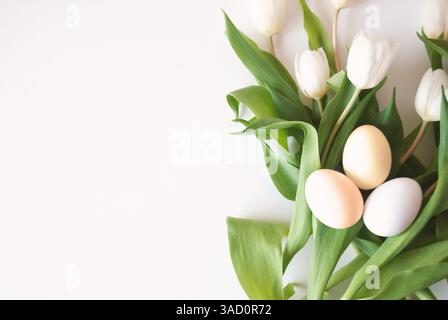 Minimalist flat lay with white tulips and pastel-colored Easter eggs on a bright white background, celebrating spring and seasonal renewal. Stock Photo