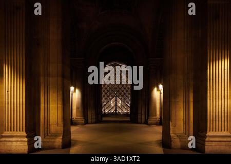 A long hallway with a large archway in the middle. The archway is lit up by lamps, creating a warm Stock Photo