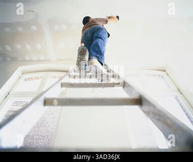 Man standing on ladder and drilling a hole into ceiling Stock Photo