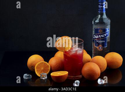 Vodka, oranges, long drink with ice cube cubes, vodka bottle in the background on a reflective background, studio shot Stock Photo