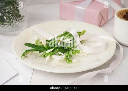 Plate with beautiful snowdrops and ribbon on white table Stock Photo