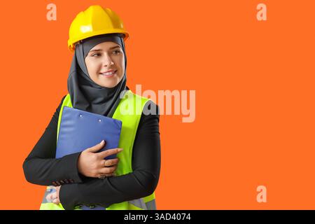 Female Muslim construction worker with clipboard on orange background Stock Photo