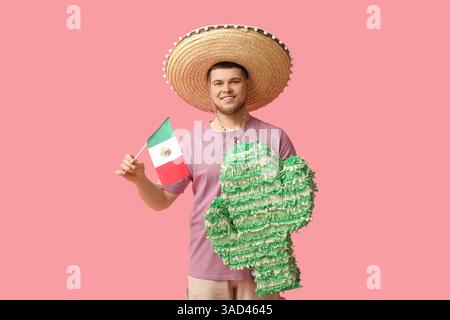 Handsome young happy man in sombrero with pinata and Mexican flag on pink background. Cinco de Mayo celebration Stock Photo